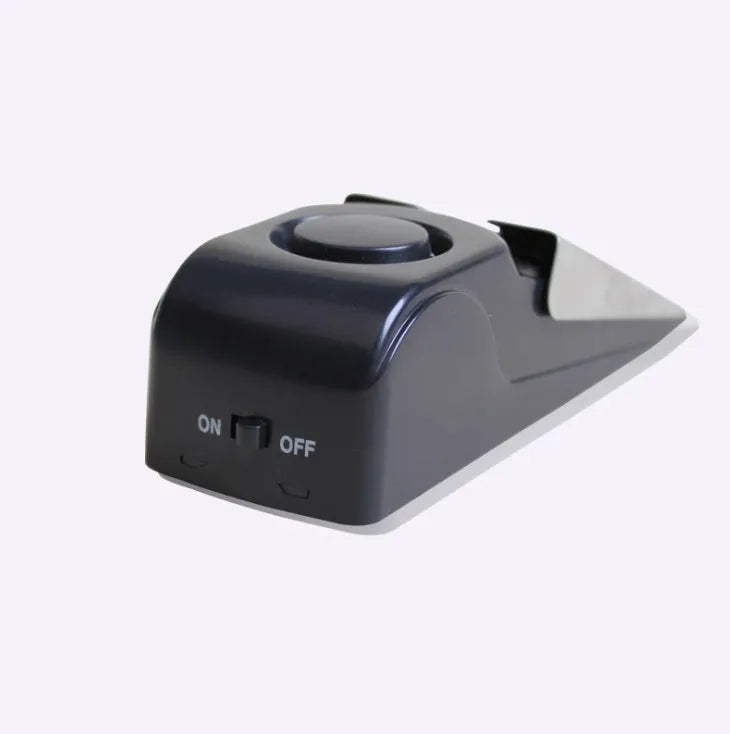 Black portable door stop alarm with wedge shape and stainless steel cover on a wooden floor.