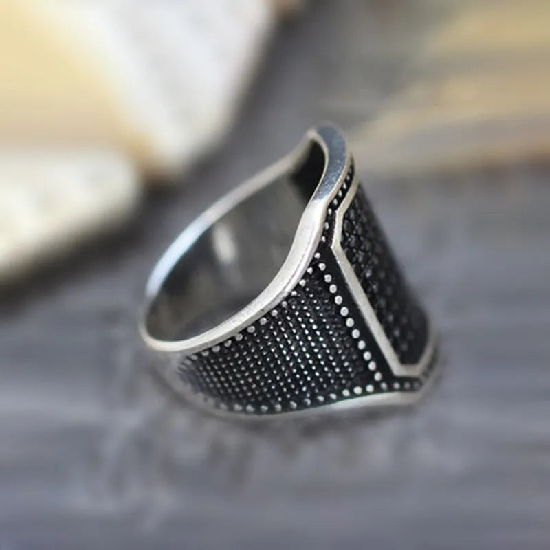 Black alloy ring with inlaid copper detail and a central zircon stone, shown on a finger.