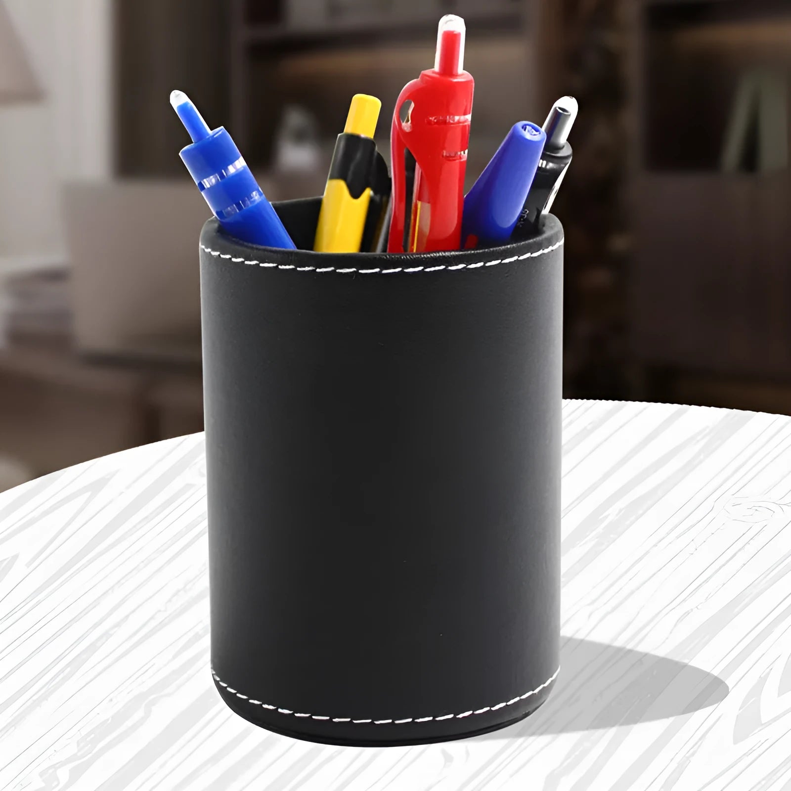 Small round black leather pen container for desk organisation.