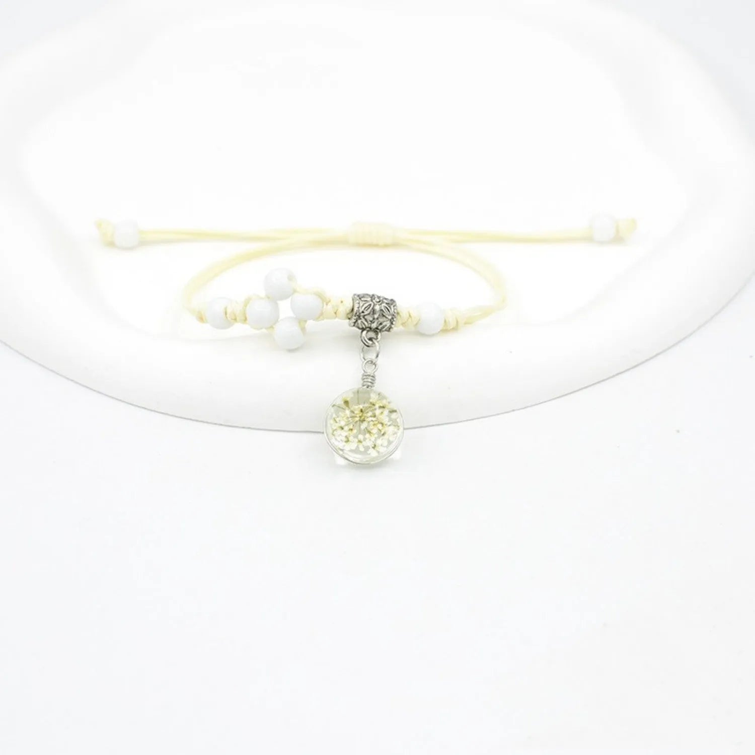 Close-up of a hand-woven glass bracelet with large 1.4cm beads containing real dried flowers and lace floral detailing.