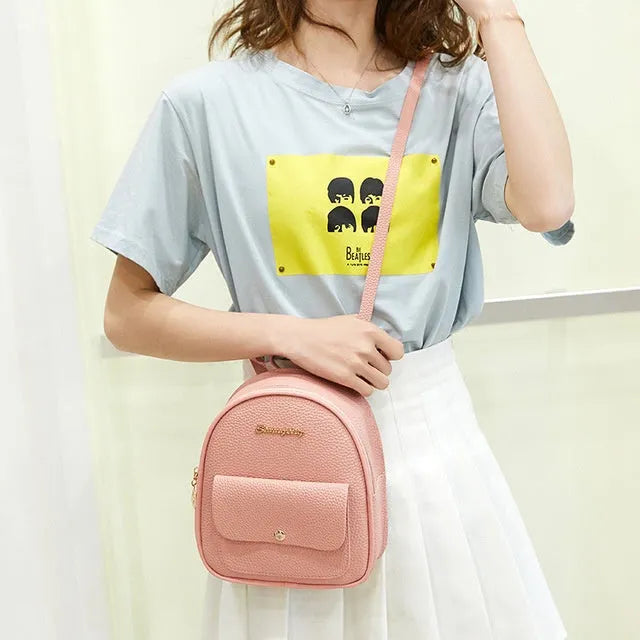 Small black PU women's backpack worn on shoulder, showing zip closure and compact size.