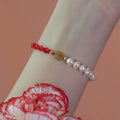Close-up of a women's pearl and braided red rope bracelet with a gold-plated geometric fu character charm.