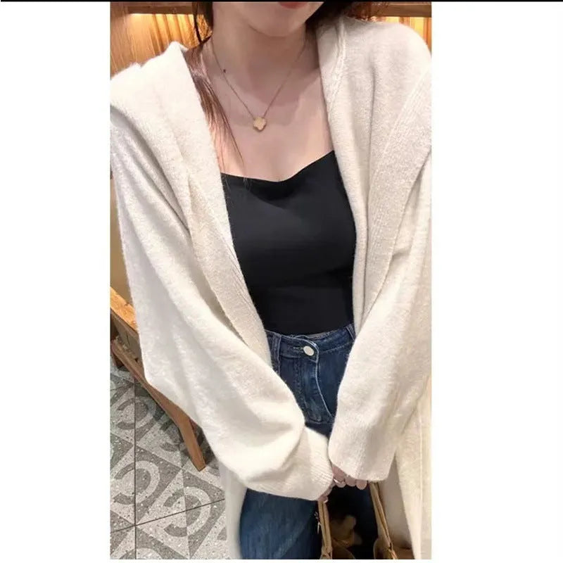 A woman wearing a long, beige, hooded knitted cardigan in a loose, below-the-knee Korean style.