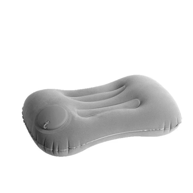 Grey inflatable travel pillow with soft flocking surface, shown deflated and next to a backpack for scale.