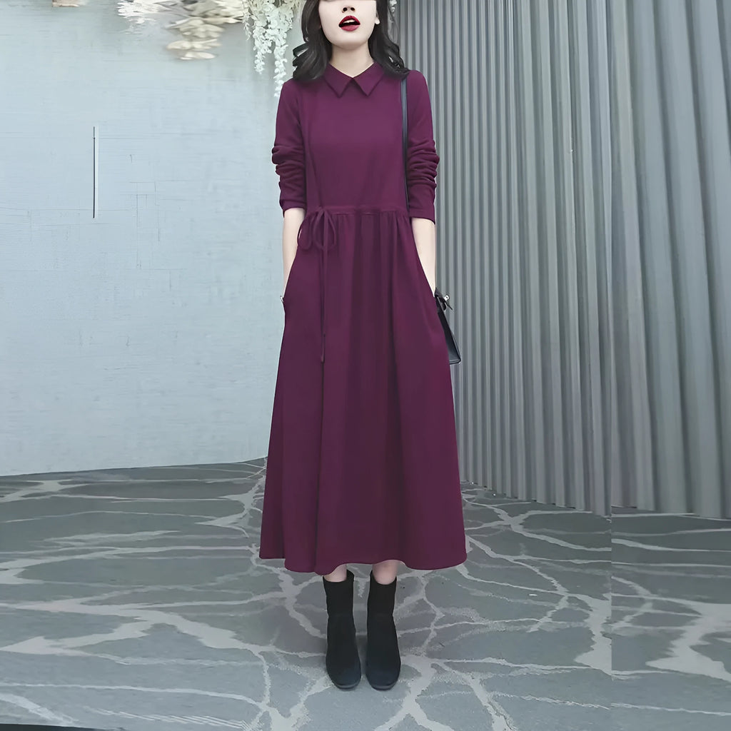 A woman wearing a solid purplish-red long-sleeve maxi dress, showcasing its extra-long sleeves and full-length skirt.