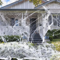 White cotton spider web Halloween decoration with plastic spiders draped over a fence.