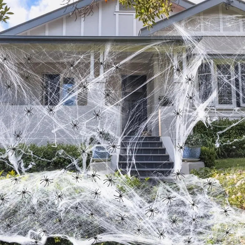 White cotton spider web Halloween decoration with plastic spiders draped over a fence.