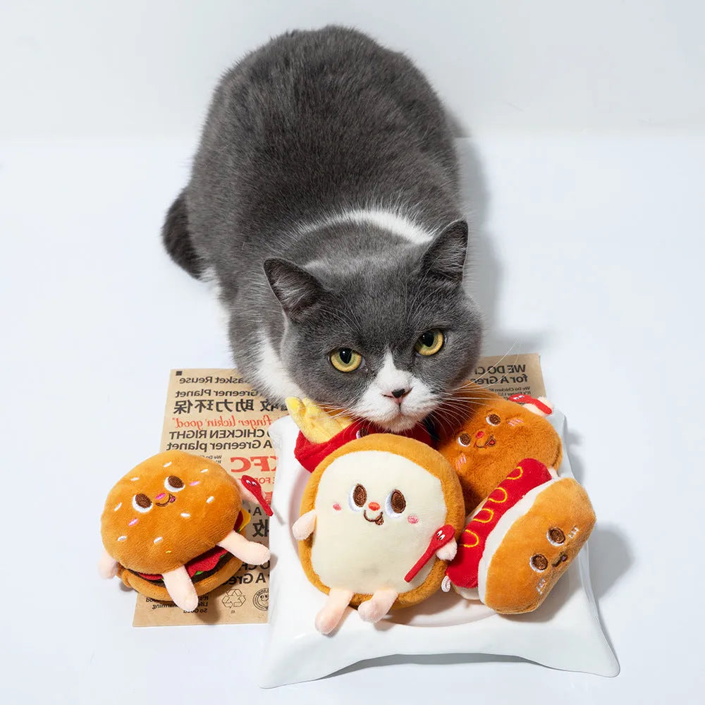 Five cat teething toys shaped like hamburger, chicken leg, fries, hot dog and bread on white background