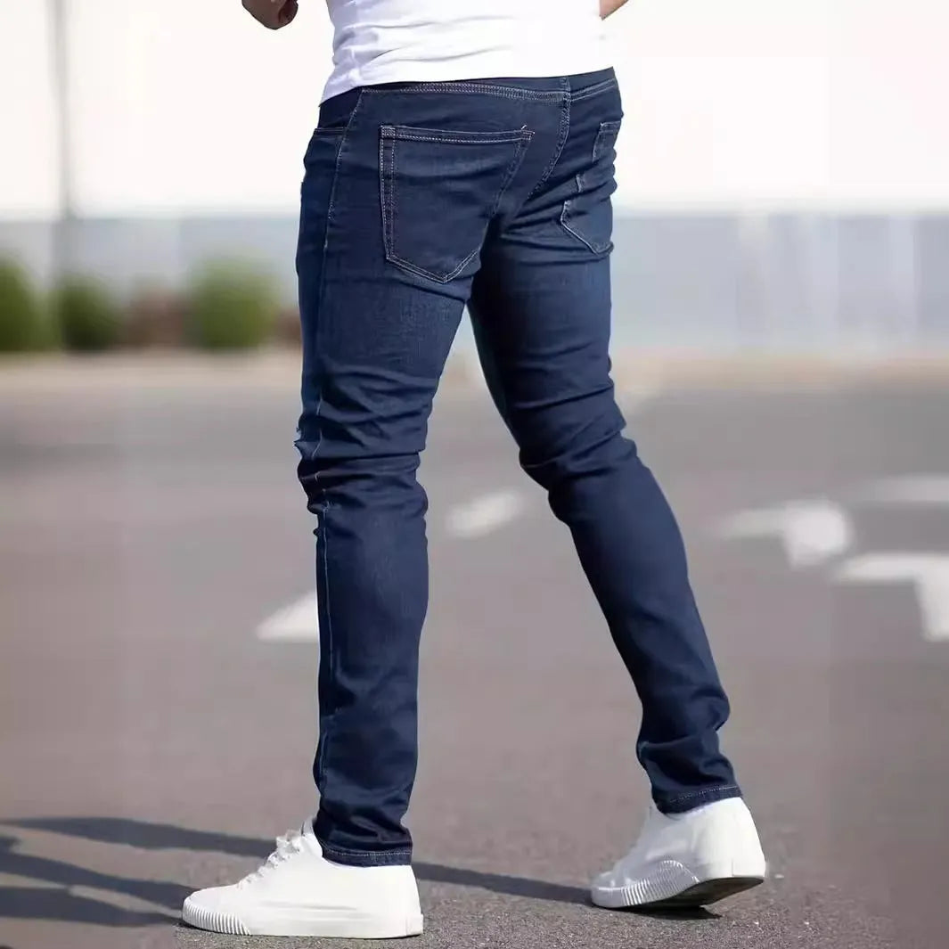 Men's dark blue skinny fit cotton jeans with a mid-rise waist and zipper fly on a plain background.