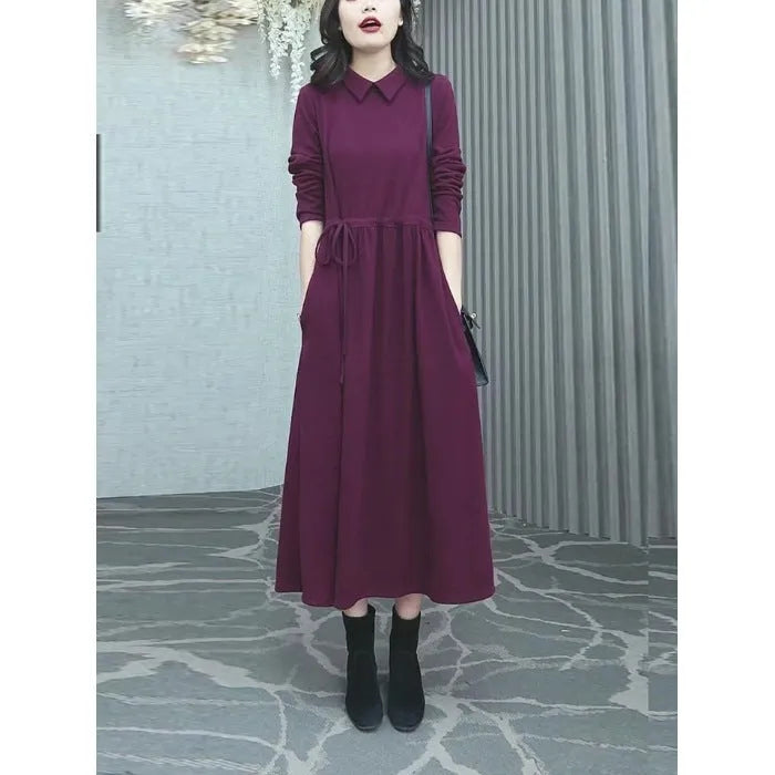A woman wearing a solid purplish-red long-sleeve maxi dress, showcasing its extra-long sleeves and full-length skirt.