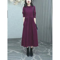 A woman wearing a solid purplish-red long-sleeve maxi dress, showcasing its extra-long sleeves and full-length skirt.