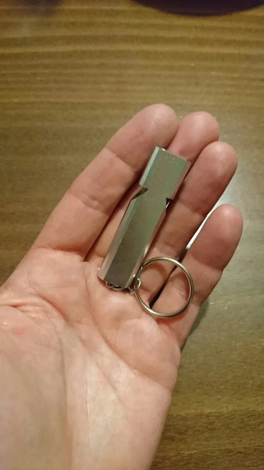 Close-up of a silver aluminium alloy double-hole outdoor survival whistle on a dark background.
