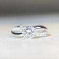 Geometric twisted silver band ring with a 1 carat round moissanite stone in a four-claw setting.