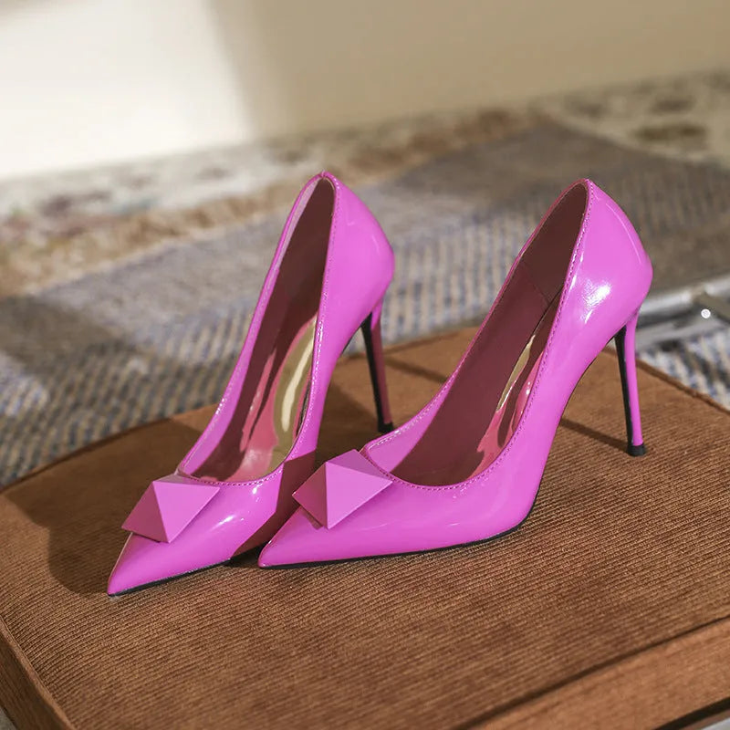Women's pink patent leather pointed toe stiletto heels with buckle and rivet detail on a shallow cut.