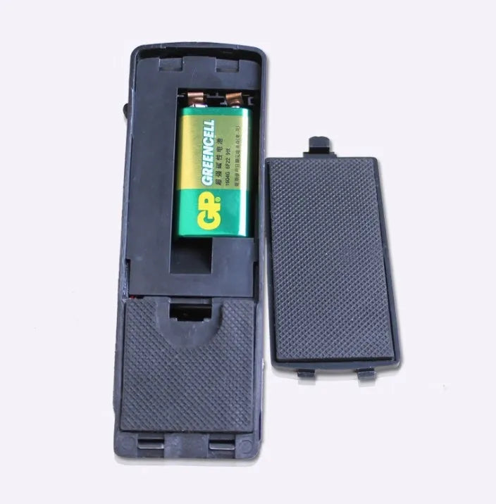 Black portable door stop alarm with wedge shape and stainless steel cover on a wooden floor.