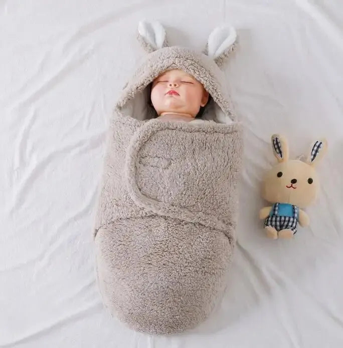 Baby wearing a blue adjustable cotton sleep sack with velcro swaddle closures and a head-protecting hood.