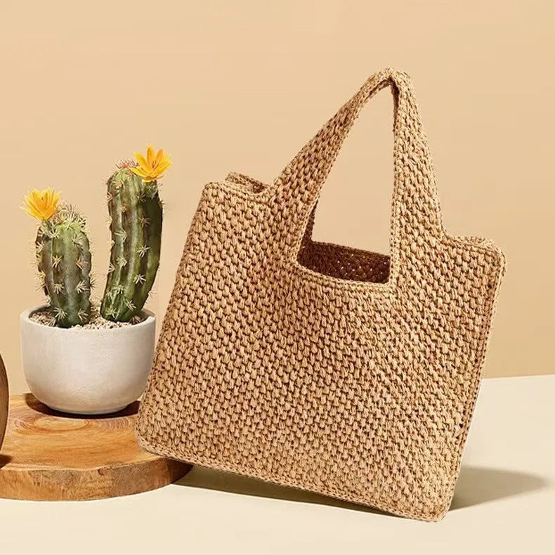 Woven straw tote bag with double shoulder straps in a horizontal square shape, shown in a neutral colour.