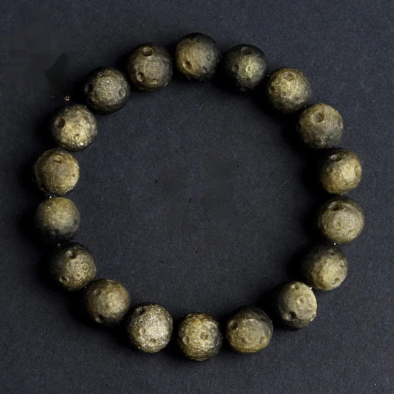 Close-up of an obsidian crater ball bead bracelet in a gold meteorite finish, showing its textured spherical beads.