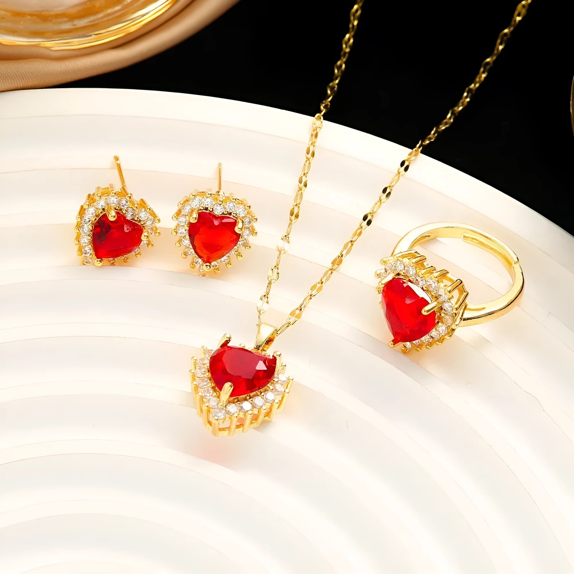 Gold red titanium steel necklace with heart and flower pendant, matching stud earrings, and ring on a grey background.
