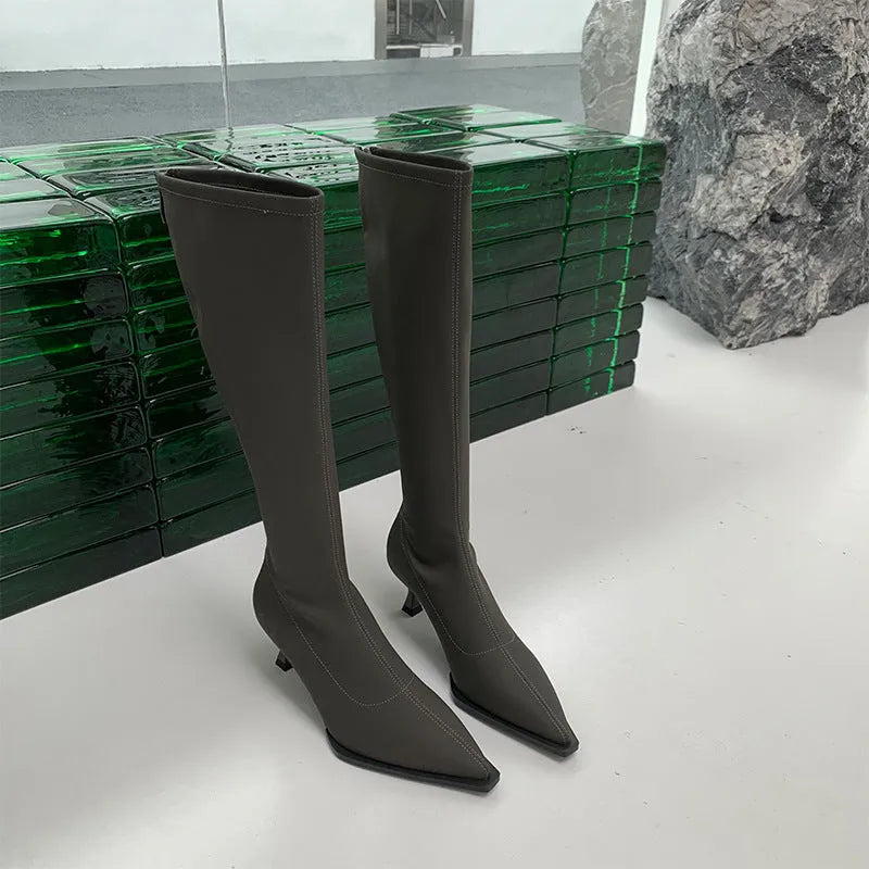 Women's black pointed toe below-the-knee boots with a stiletto heel and back zip on a neutral background.