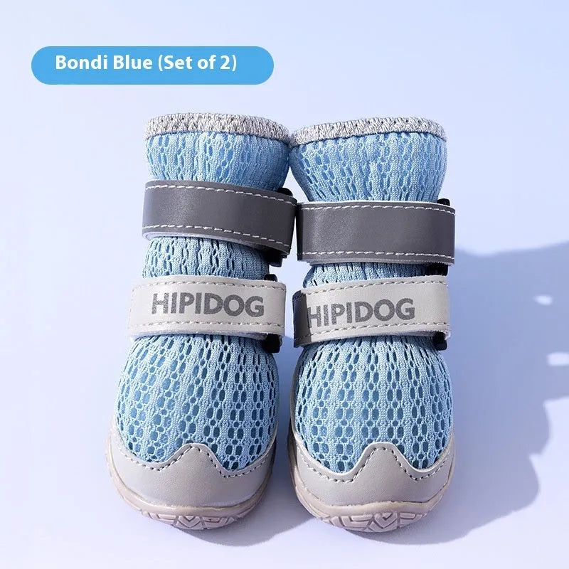 Pair of light blue breathable dog shoes with a cartoon style on a wooden floor.