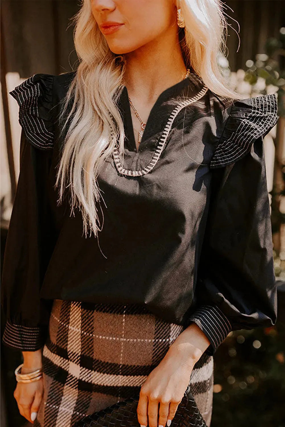 Black women's V-neck long sleeve blouse with white contrast stitching and a ruffle cuff detail