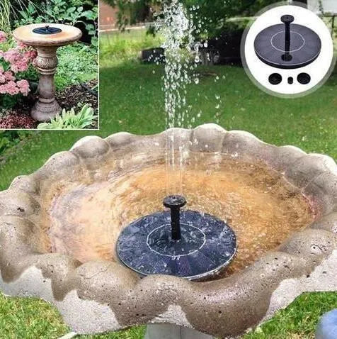 Black solar fountain pump with four spray nozzles on a green grass background next to a birdbath.