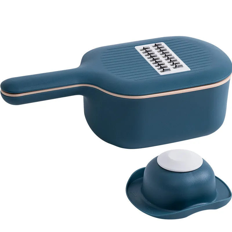 Dark blue vegetable cutter with four stainless steel blades, a hand guard, and a drain basket on a kitchen counter.