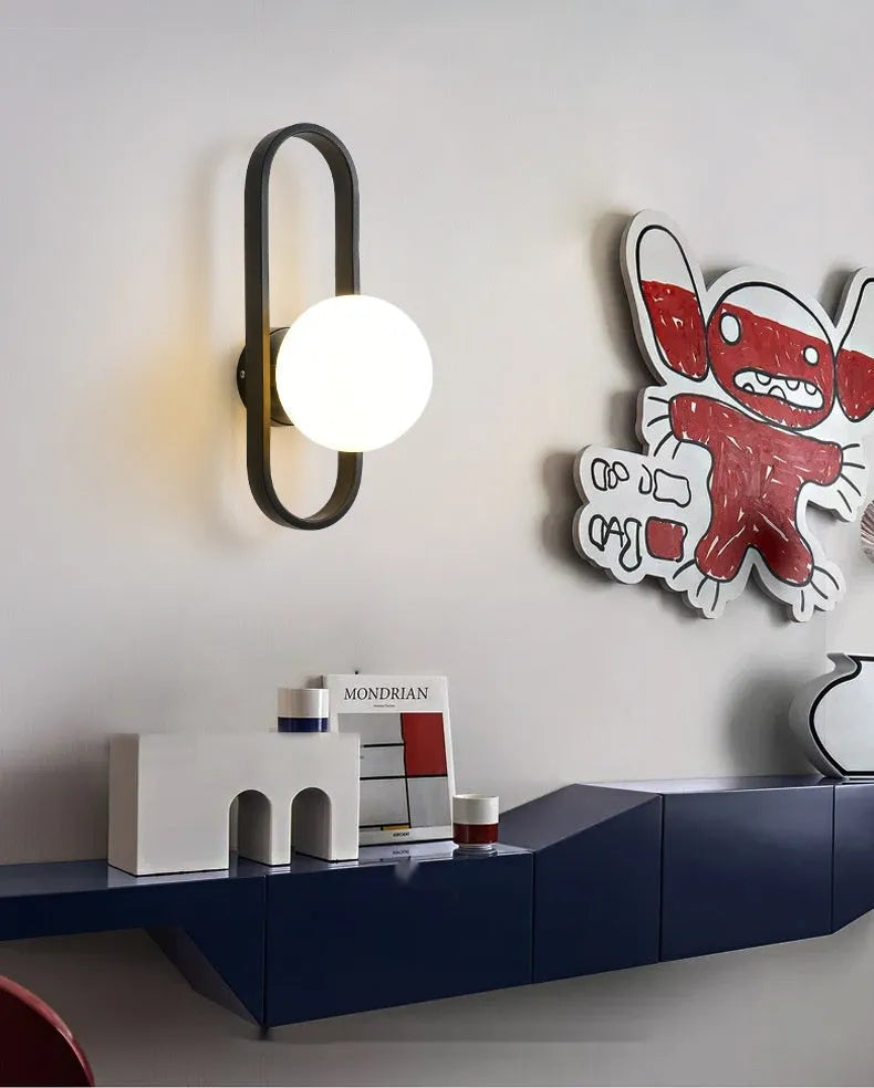 Modern minimalist wall lamp with black iron arm and clear glass shade, mounted on a plain wall.