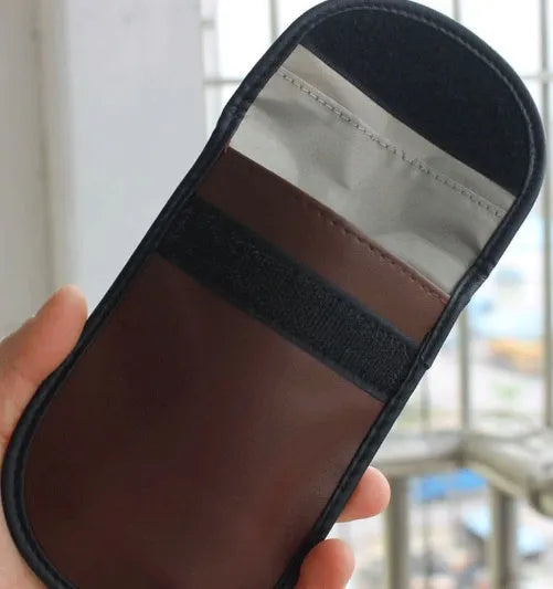 Black microfiber Faraday cage pouch for blocking car key and RFID card signals on a table.