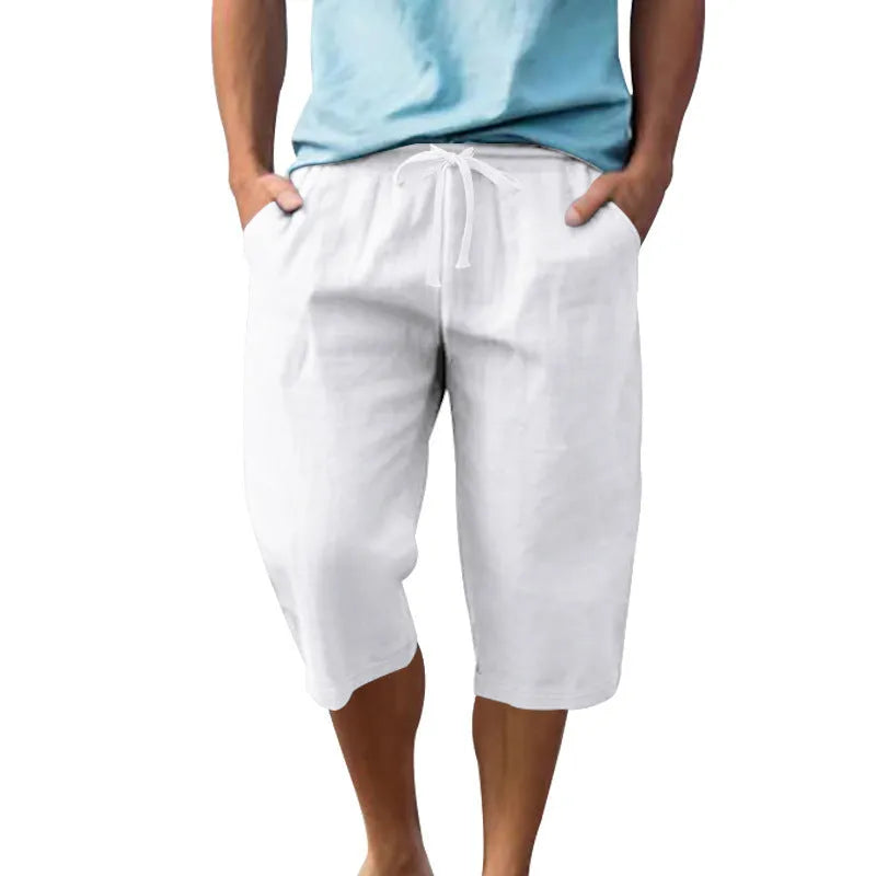 Man wearing loose-fit, solid-colour linen shorts in a light blue shade, showing the cropped length and drawstring waist.