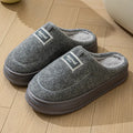 Men's brown suede slippers with a thick, textured sole on a wooden floor