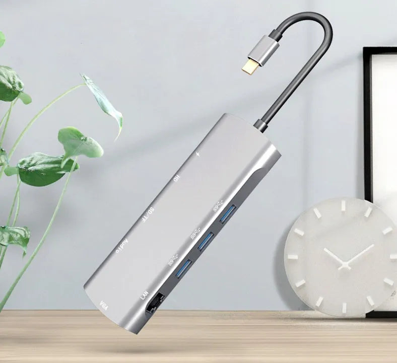 Grey aluminium USB-C docking station with HDMI, VGA, USB 3.0, and PD charging ports on a desk.