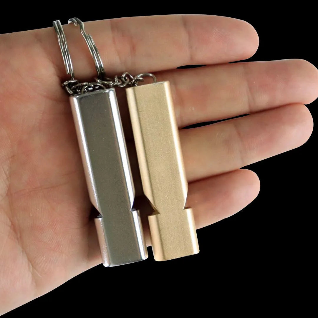 Close-up of a silver aluminium alloy double-hole outdoor survival whistle on a dark background.