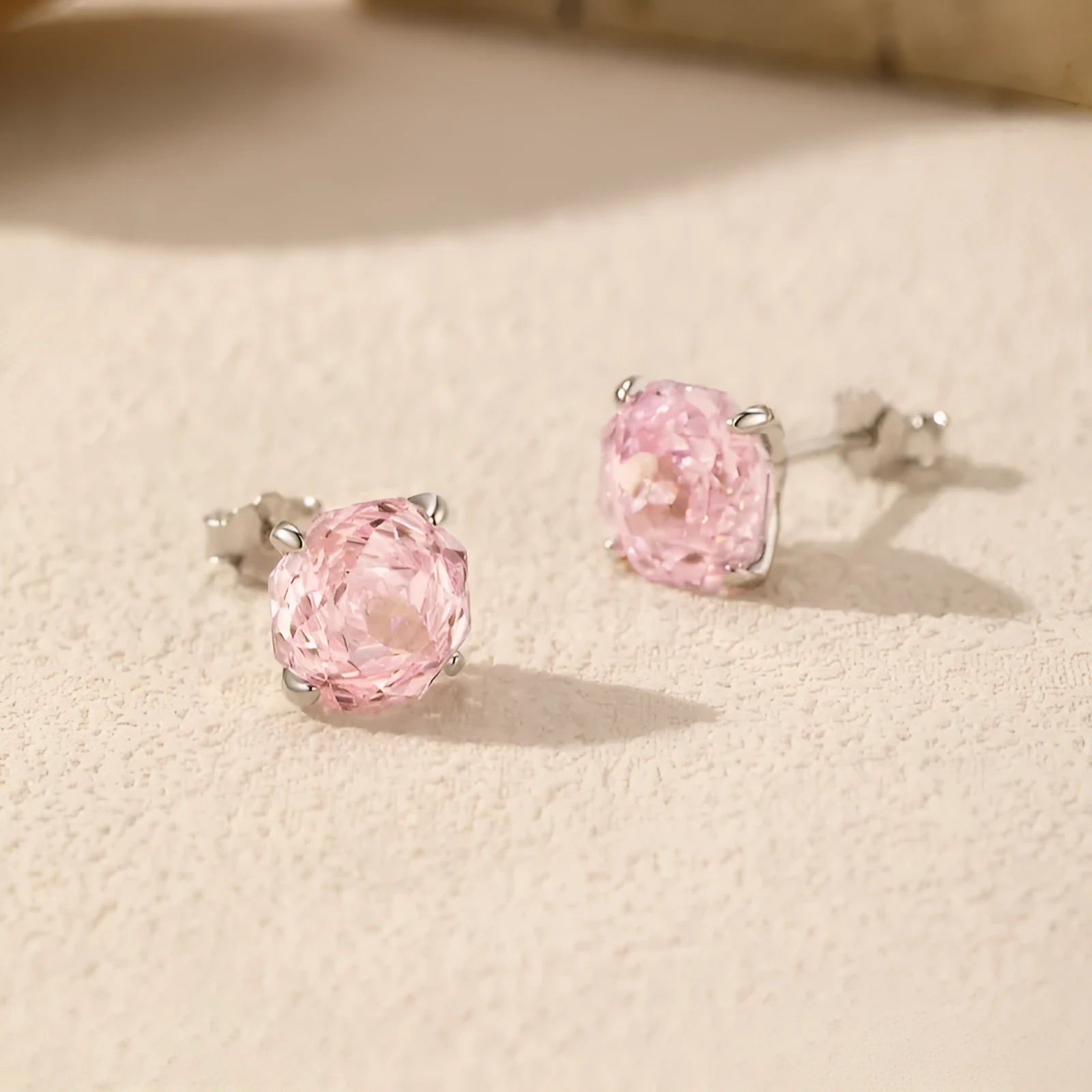 Close-up of a pair of pink S925 sterling silver rose-shaped stud earrings on a plain background.