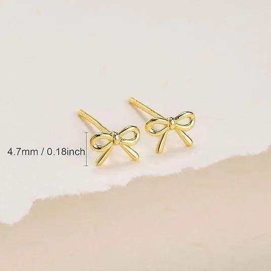 Women's gold bow stud earrings and silver cross stud earrings on a flat surface.