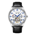 Men's stainless steel mechanical watch with leather strap and butterfly buckle on a business suit cuff.