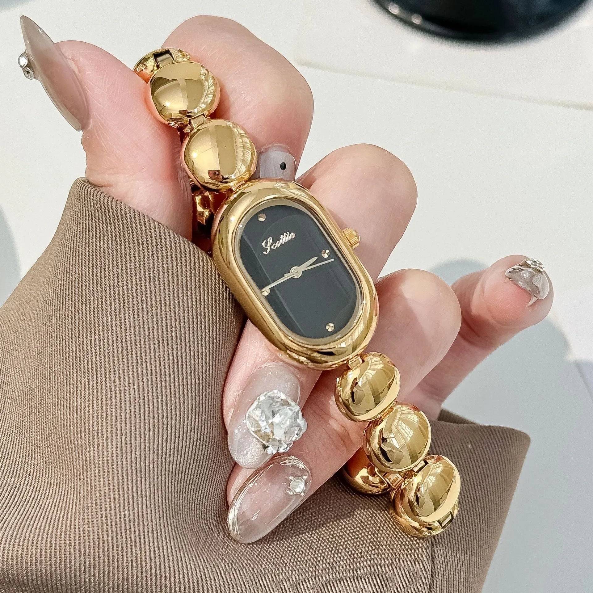 Oval women's fashion watch on wrist showing 9mm thick case, available in black gold, platinum and other colours.