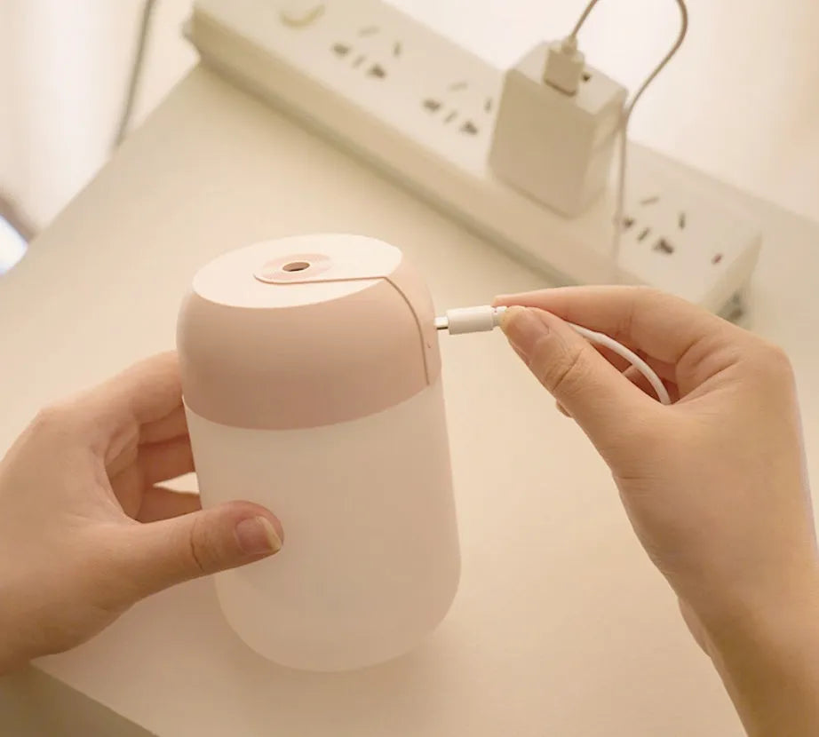 White cylindrical mini humidifier with USB cable on a wooden surface.