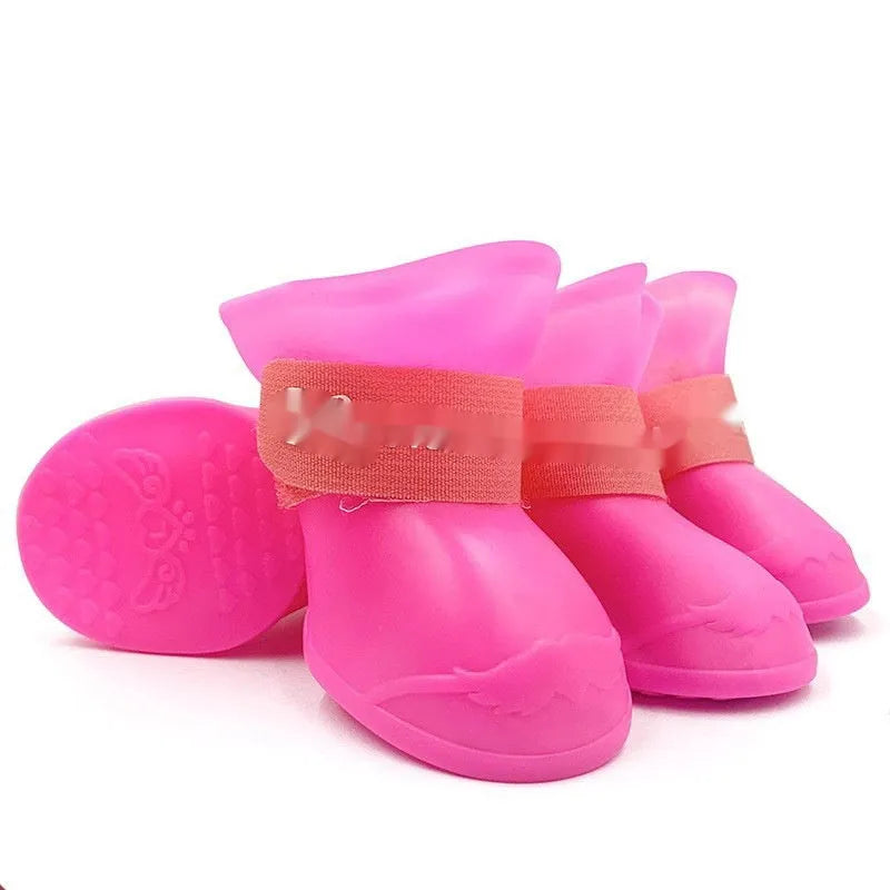 Set of four colourful rubber dog rain shoes with anti-slip soles on a wet surface.