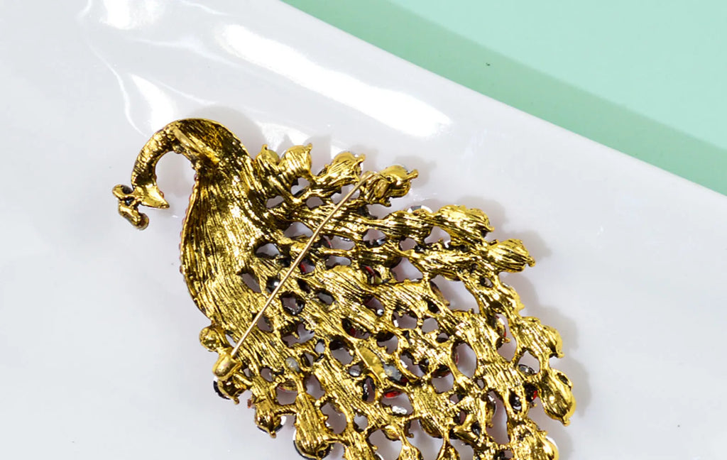Colourful metal peacock brooch in red, green, and blue with rhinestone accents on a white background