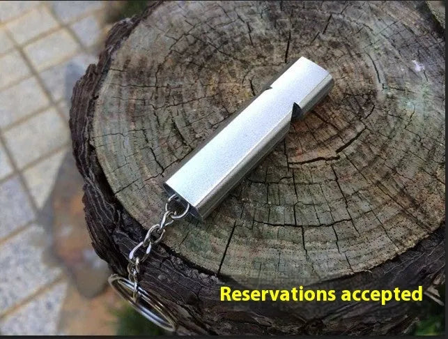 Close-up of a silver aluminium alloy double-hole outdoor survival whistle on a dark background.