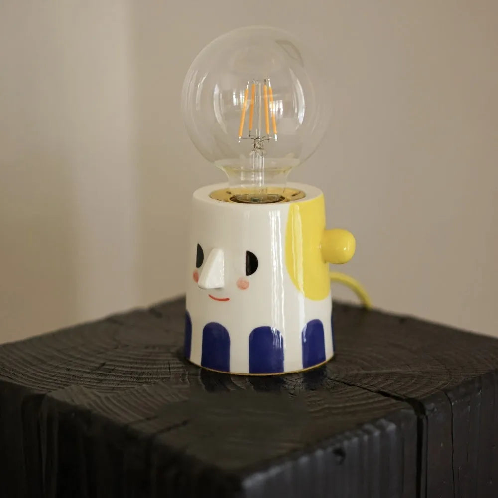 Handmade ceramic bedside lamp with white ball headlight shade on a wooden table.