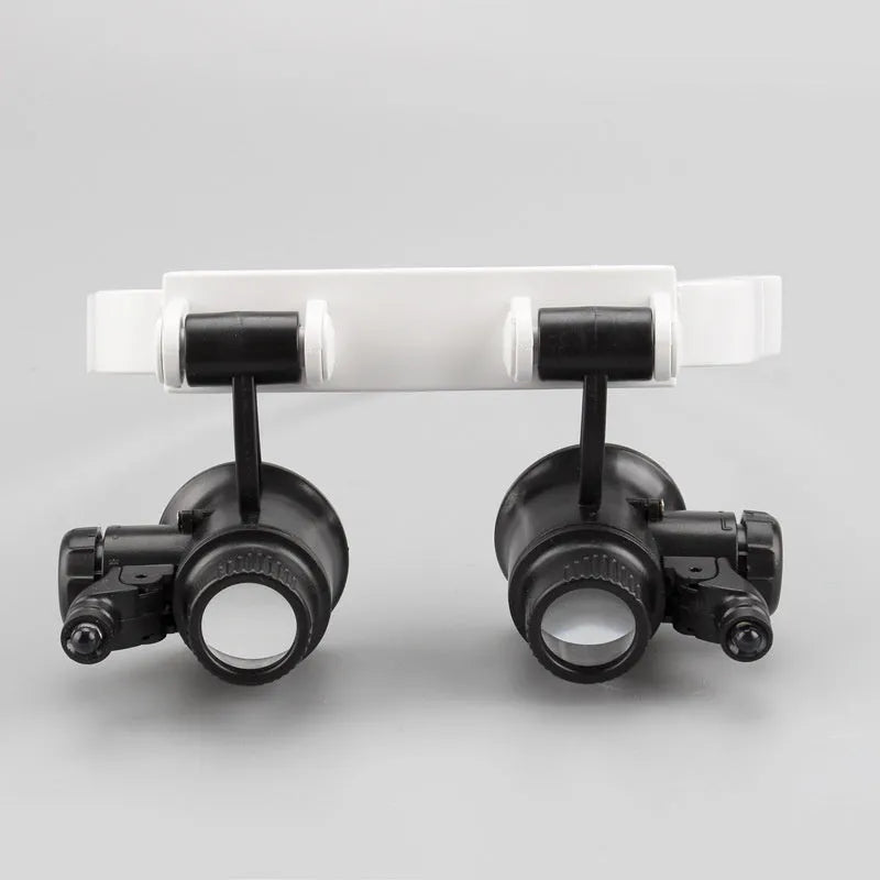White head-mounted magnifying glass with LED light, shown folded and unfolded on a workbench.