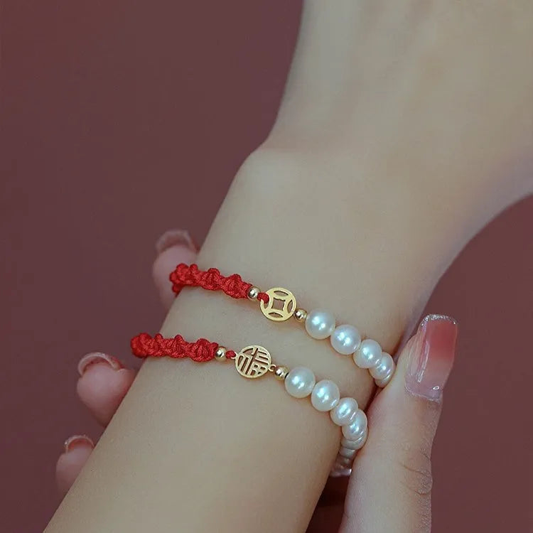 Close-up of a women's pearl and braided red rope bracelet with a gold-plated geometric fu character charm.