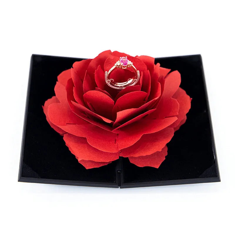 Red heart-shaped rotating ring box with 3D white rose decoration on top.