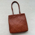 Brown handmade woven leather tote bag with a three-dimensional front pocket and shoulder strap.
