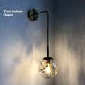 Modern small glass wall lamp in golden flower finish mounted on a bedroom wall.