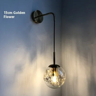 Modern small glass wall lamp in golden flower finish mounted on a bedroom wall.