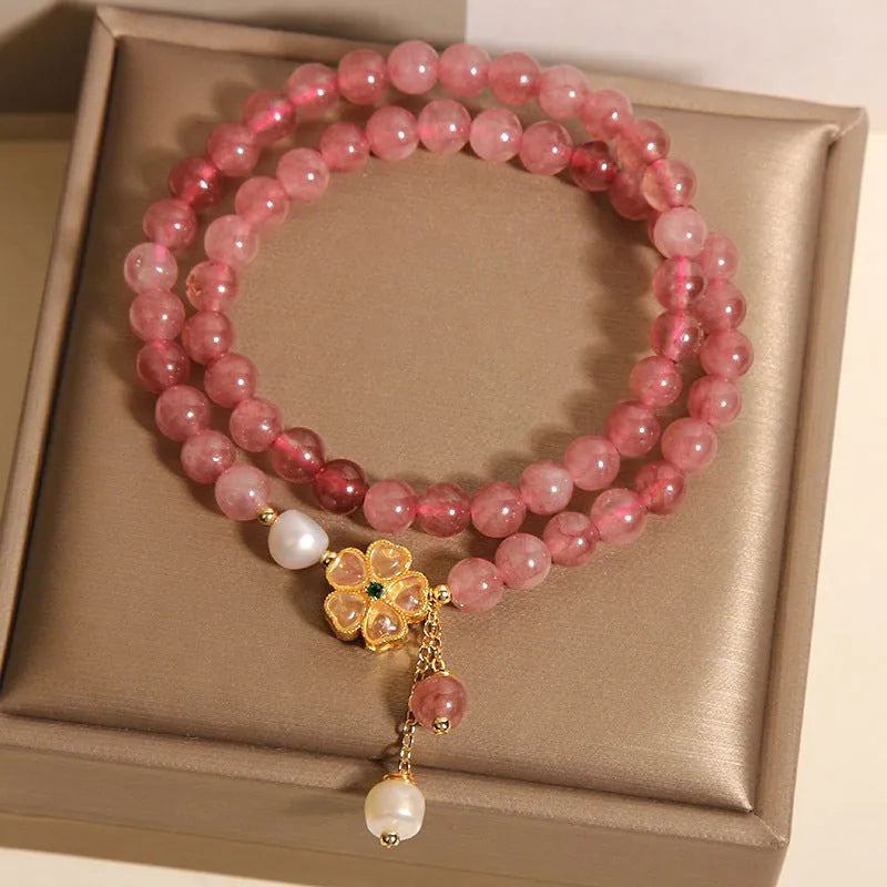 Women's double ring bracelet with strawberry quartz four-leaf clover charms on wrist.
